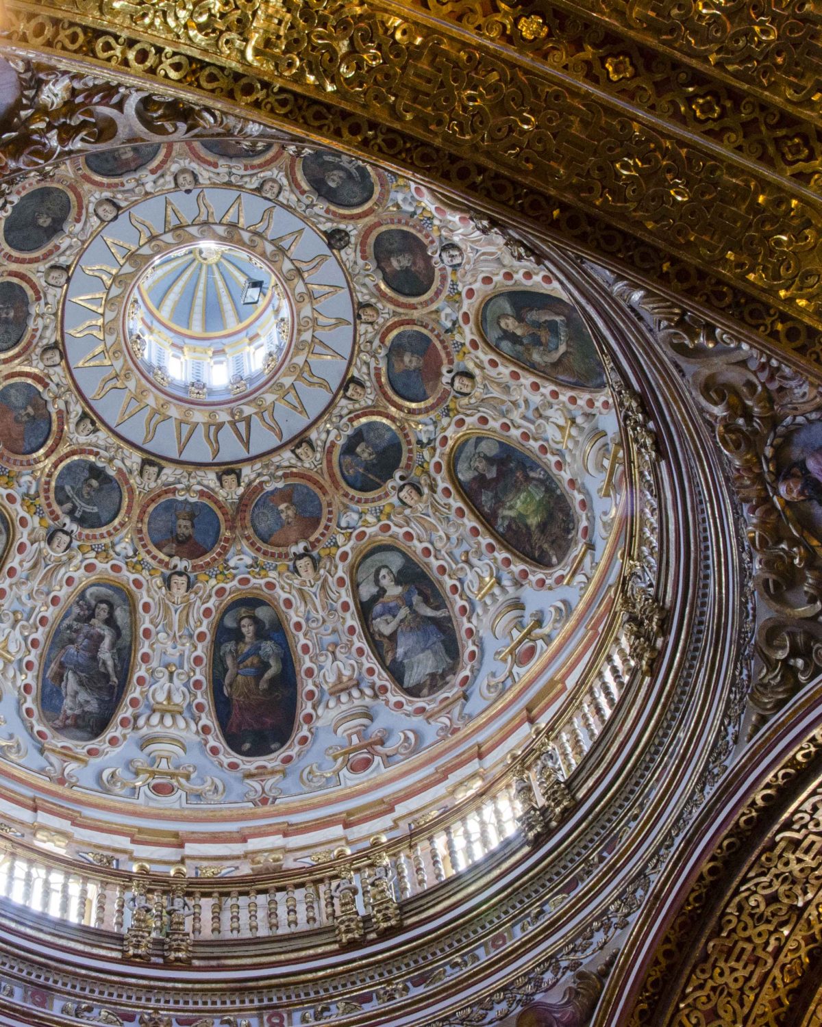 This is the central dome above just in front of the main altar, La Compania de Jesus, Quito | ©Angela Drake Looking up at the central dome in tones of light blue, dark portraits, and gold trim