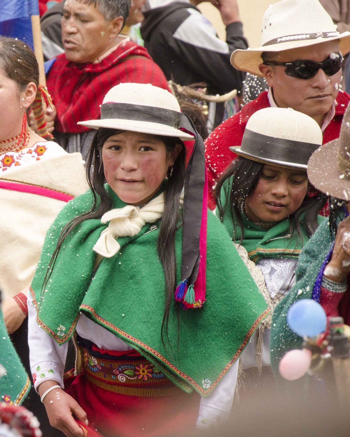 Young woman dressed in green woold shawl with white wool hat bedecked in black and red ribbons