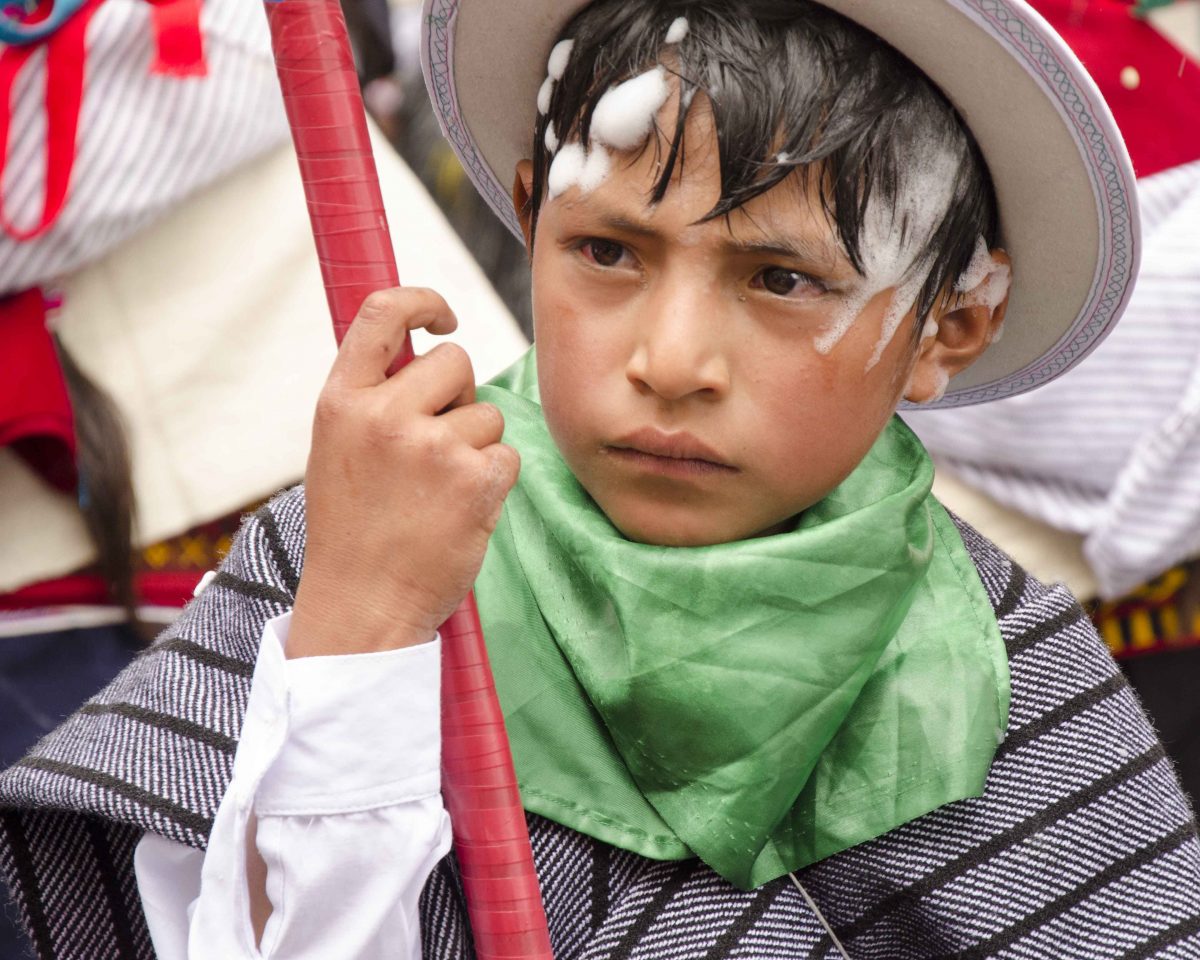 Young boy with serious face is dressed in gray poncho and white wool hate