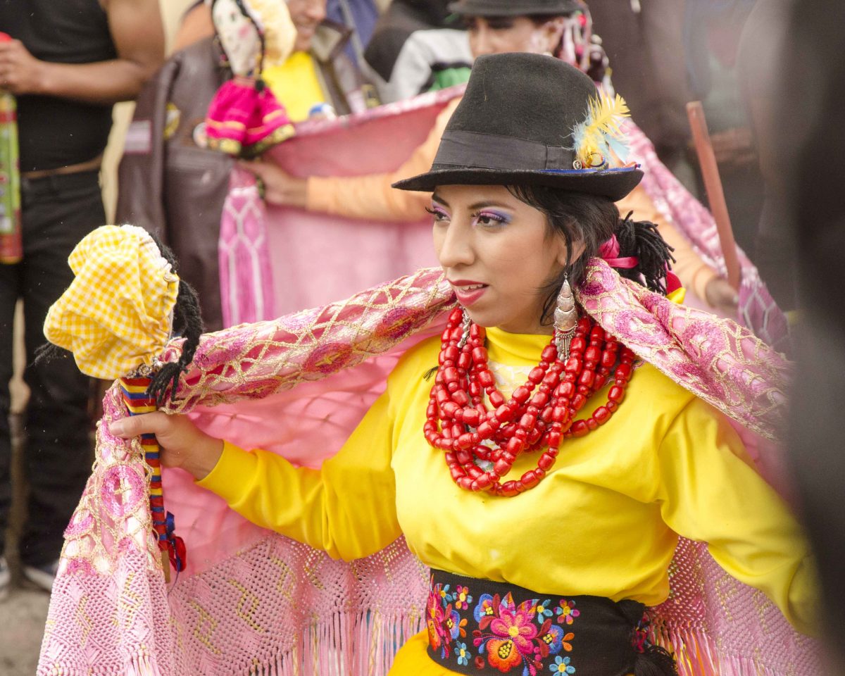 Dancer dressed in bright yellow shirt, pink shawl, and heavy red necklace also wears a dark brown felt hat, Carnaval in Guamote