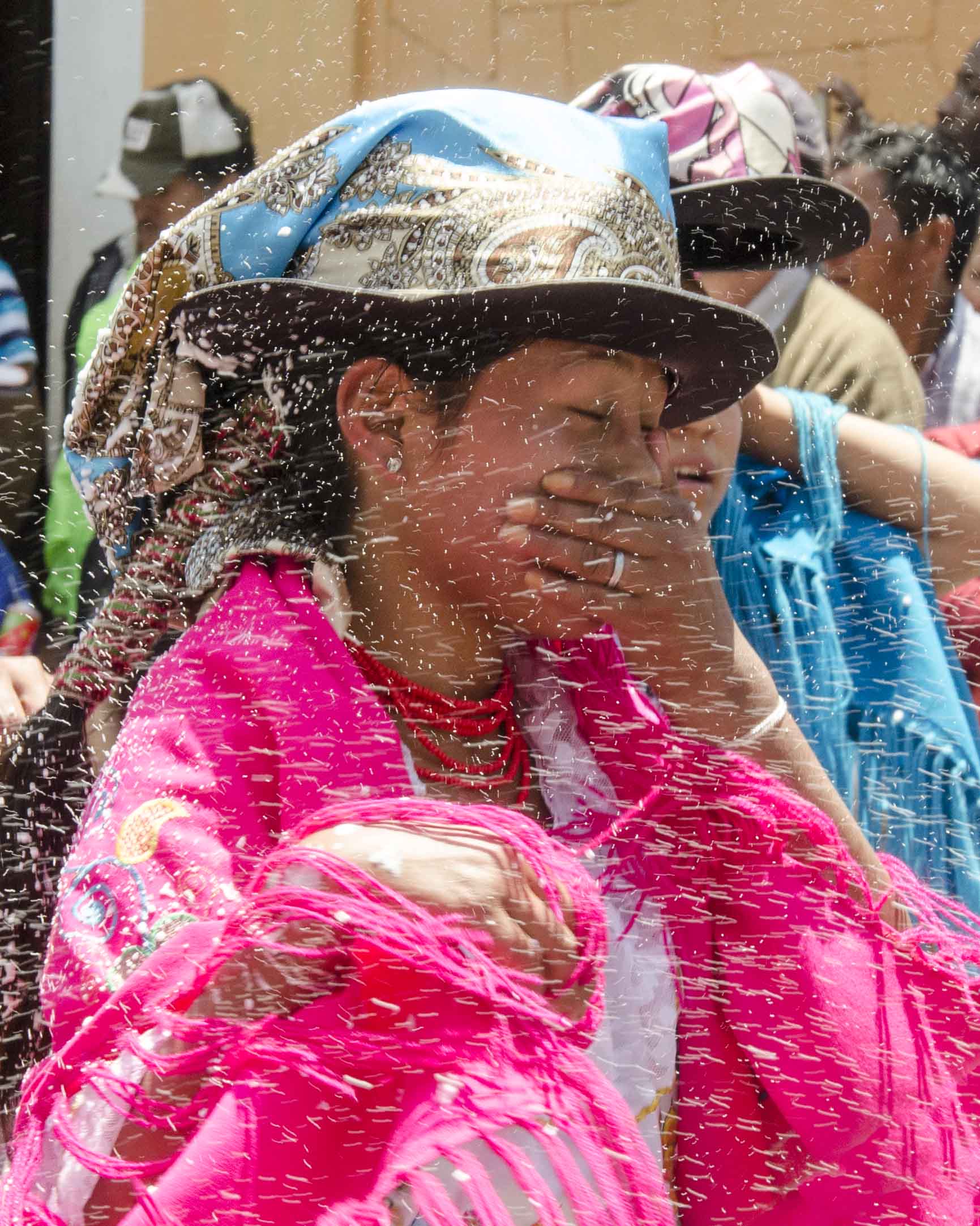 A dancer covers her face to avoid getting carioca, or party foam, in her mouth; Guaranda, Ecuador | ©Angela Drake Carnival in Guaranda, Ecuador