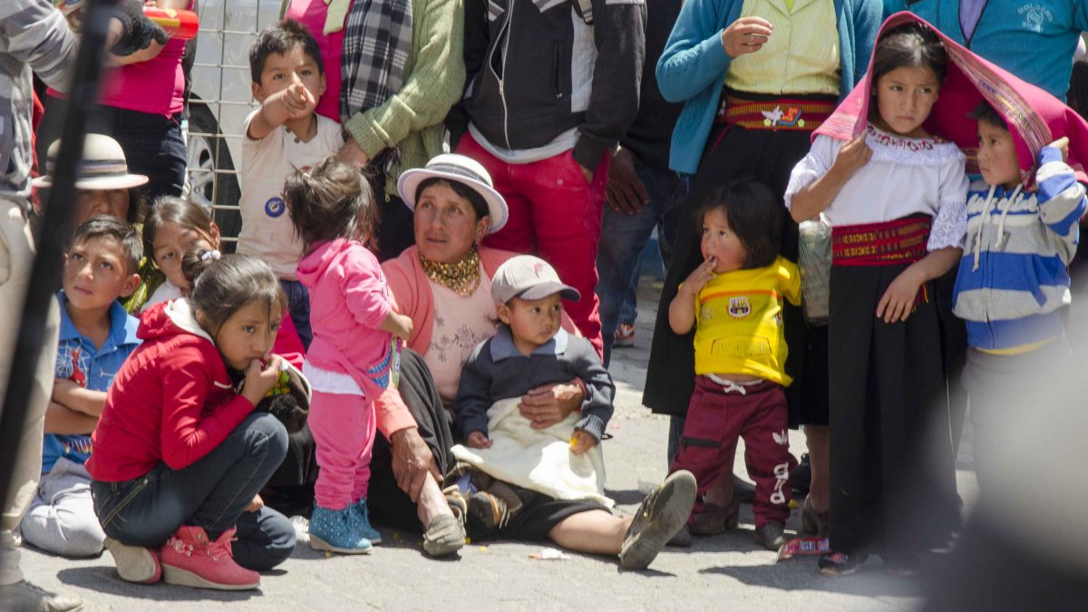 Parades are a family affair and when you have lots of little ones, sometimes it is easier to just sit down on the street than to stand on the sidewalk | ©Angela Drake Family watching the parade, Carnaval in Guaranda, Ecuador