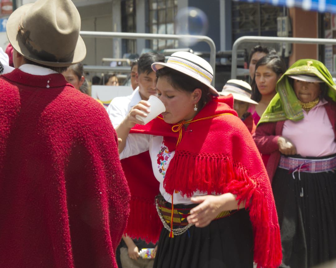 Woman in red, wool shawl drinking from a paper cup