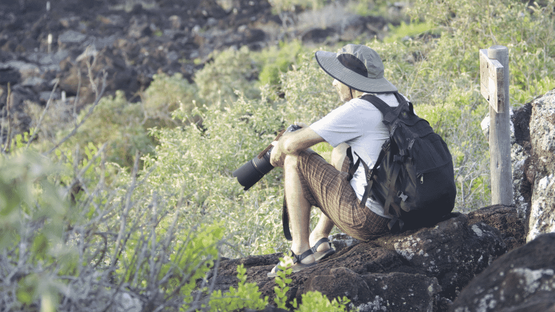 A man sits on a rock and looks out towards a view we cannot see