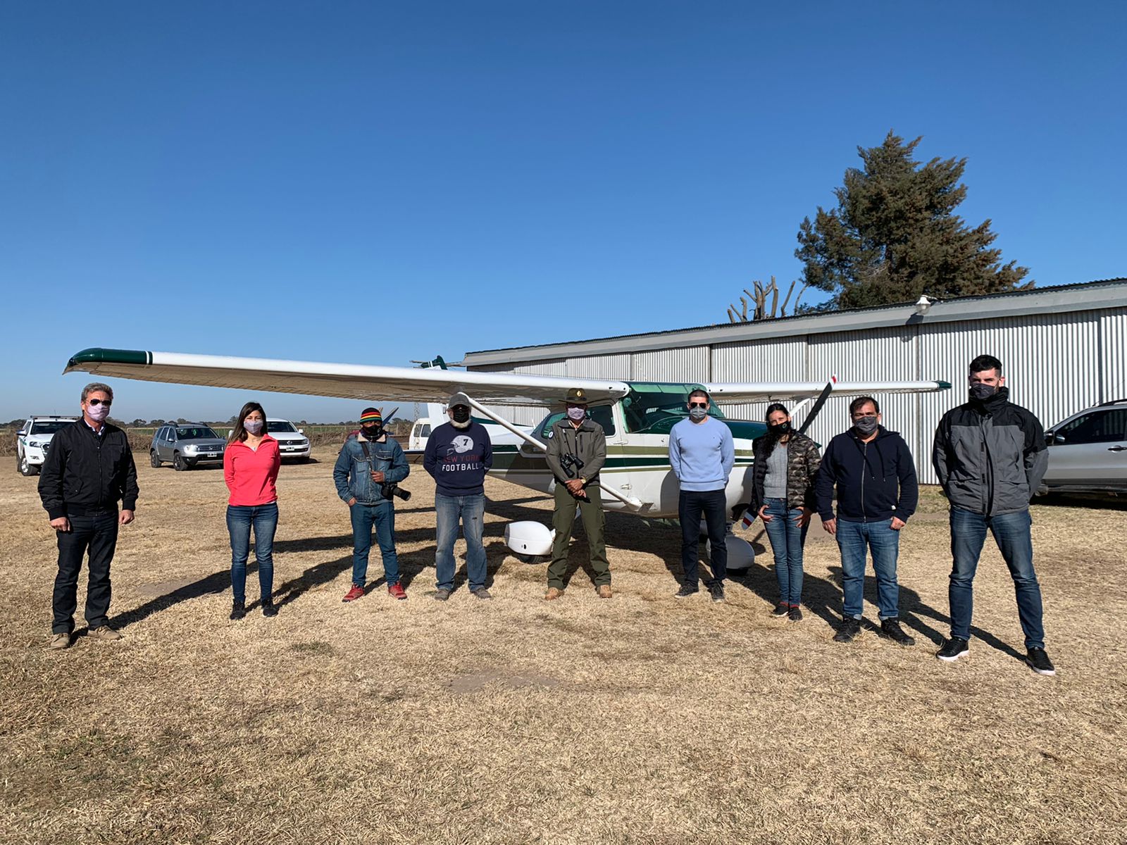 A team of eight people stand in front of a small plane