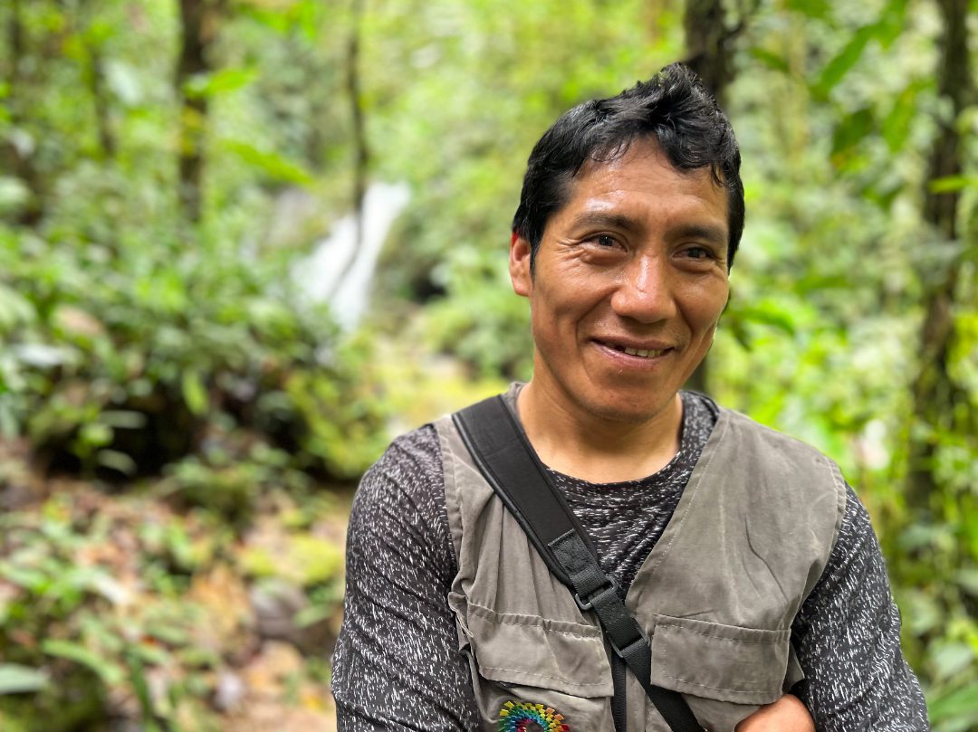 A man with a huge smile on his face poses with the green forest in the background