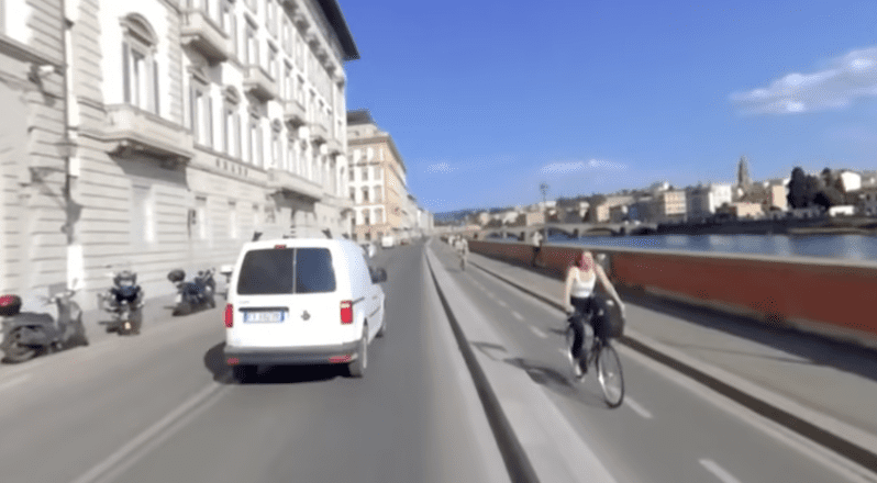 360 Intro Video A woman on a bicycle comes toward the viewer in a bike lane to the right while we follow a white van on the main road ahead