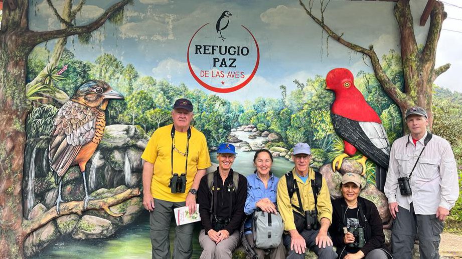 A small group of people sit in front of a mural with a giant antpitta