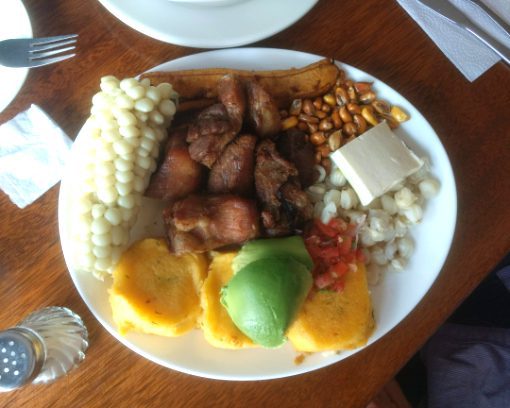 A full fritada plate including fried pork, potato patties, corn on the cob, toasted corn, hominy, cheese and avocado