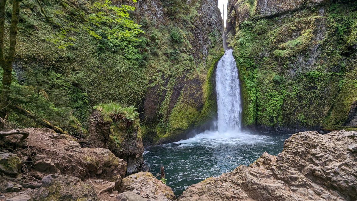 A horsetail waterfall in heavy flow falls down mossy crevace into a deep pool of crystal clear water