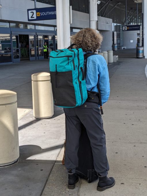 A woman wearing a travel backpack with waist belt stands at ease waiting for her ride.