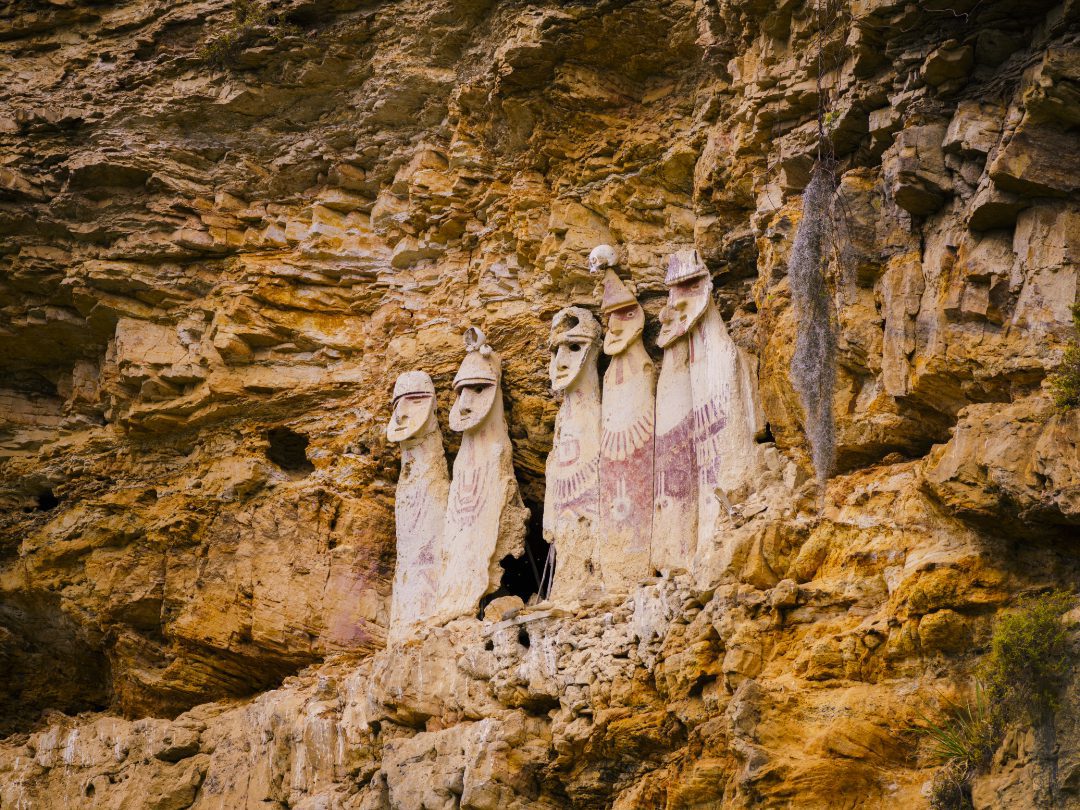 Sarcophagi of Karajía perched high on a cliffside, ancient Chachapoya burial statues standing against the rugged rock face overlooking the valley below.