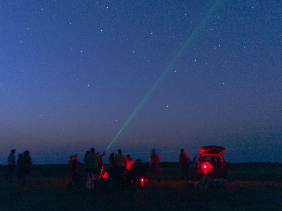 A green laser point into the deepening sky as people gather to learn about the stars