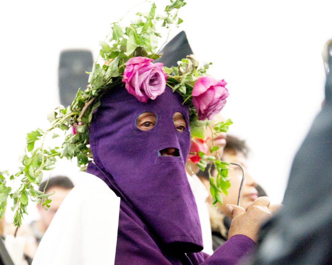 A penitent wears a purple hood adorned with a rose crown