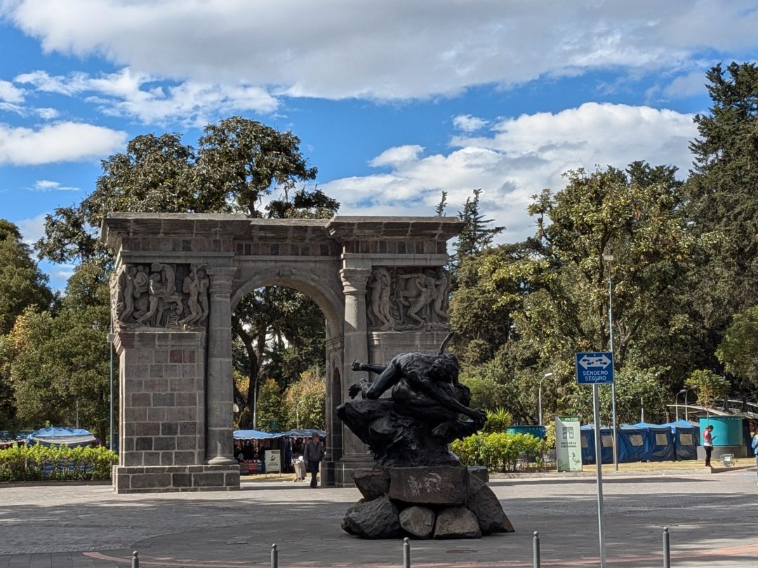 Una gran puerta de piedra y una estatua marcan la entrada principal al Parque El Ejido en Quito.