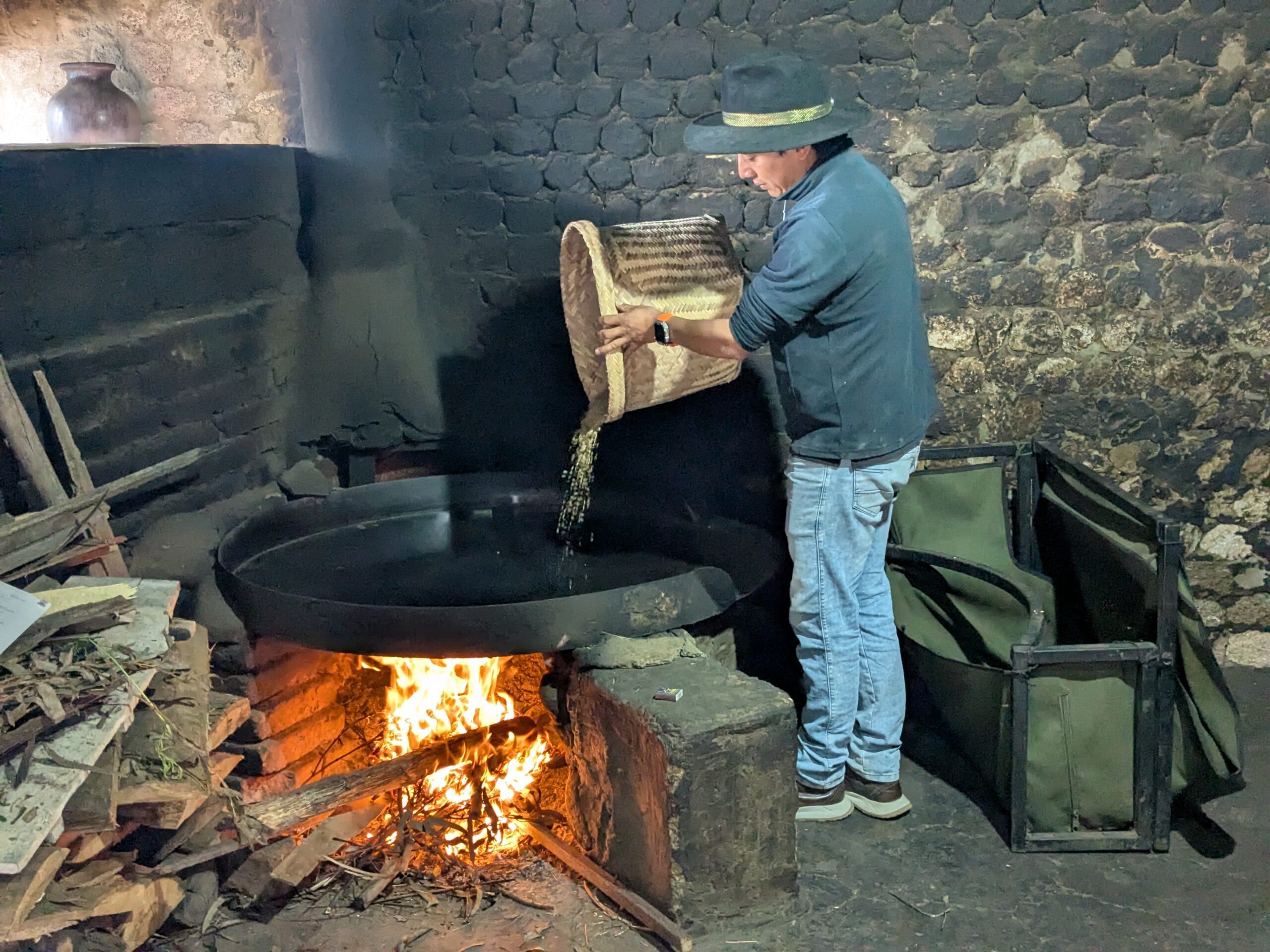 Freddy Molino pours barley from a handwoven basket onto a hot, metal pan above a wood burning fire.
