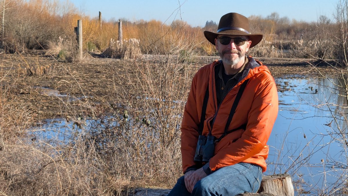 Scott wearing a bright orange Craft Sportswear Men's ADV Explore Lightweight Jacket while birdwatching at Fernhill Wetlands in Forest Grove, Oregon