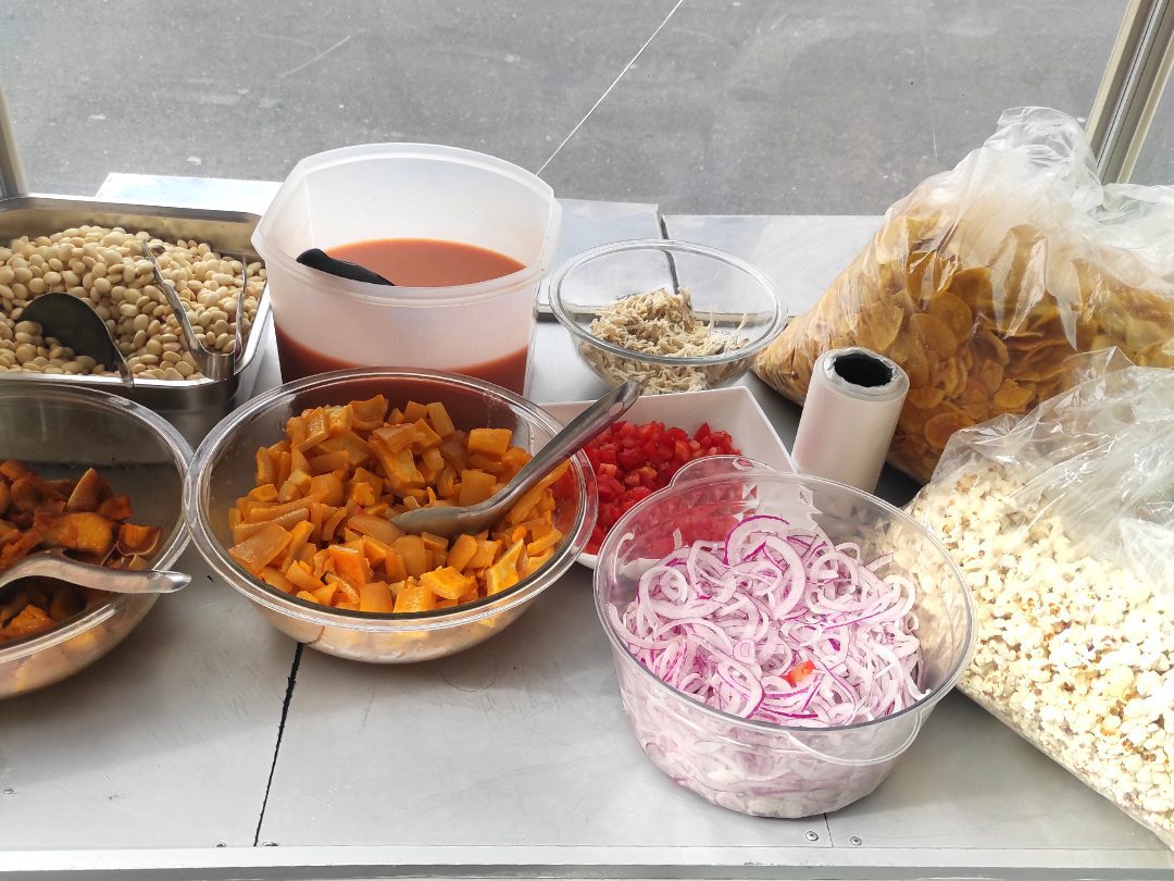 Ingredientes frescos para preparar cevichocho en un puesto local: chochos, cebolla, tomate, pollo desmenuzado, salsa de tomate, chifles y canguil.