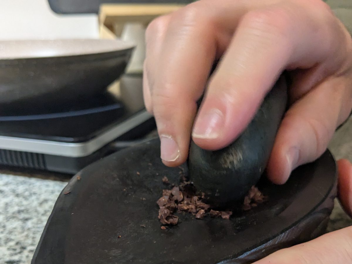 Grinding chocolate by hand. Close-up of a hand holding a mortar while grinding cacao beans on a flat pestle.