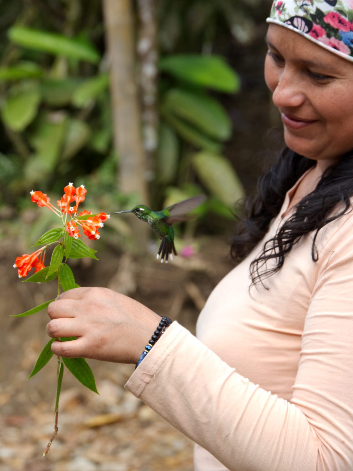 Doris, co-owner of Mashpi-Amagusa, observes a hummingbird sipping nectar from a native flower she holds in her hand.