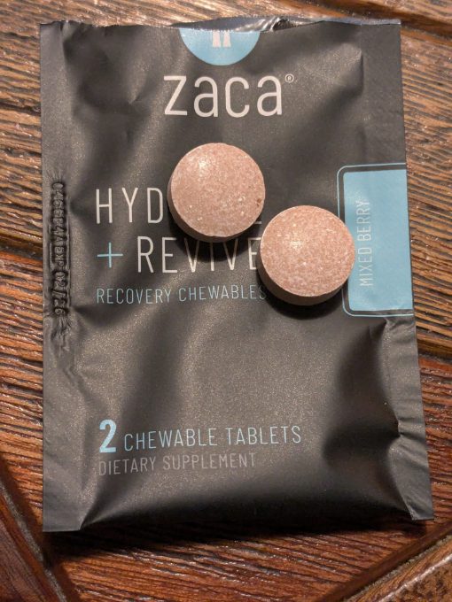 Two mixed berry tablets sit on an open Zaca Recovery Chewable package for Altitude Sickness relief.