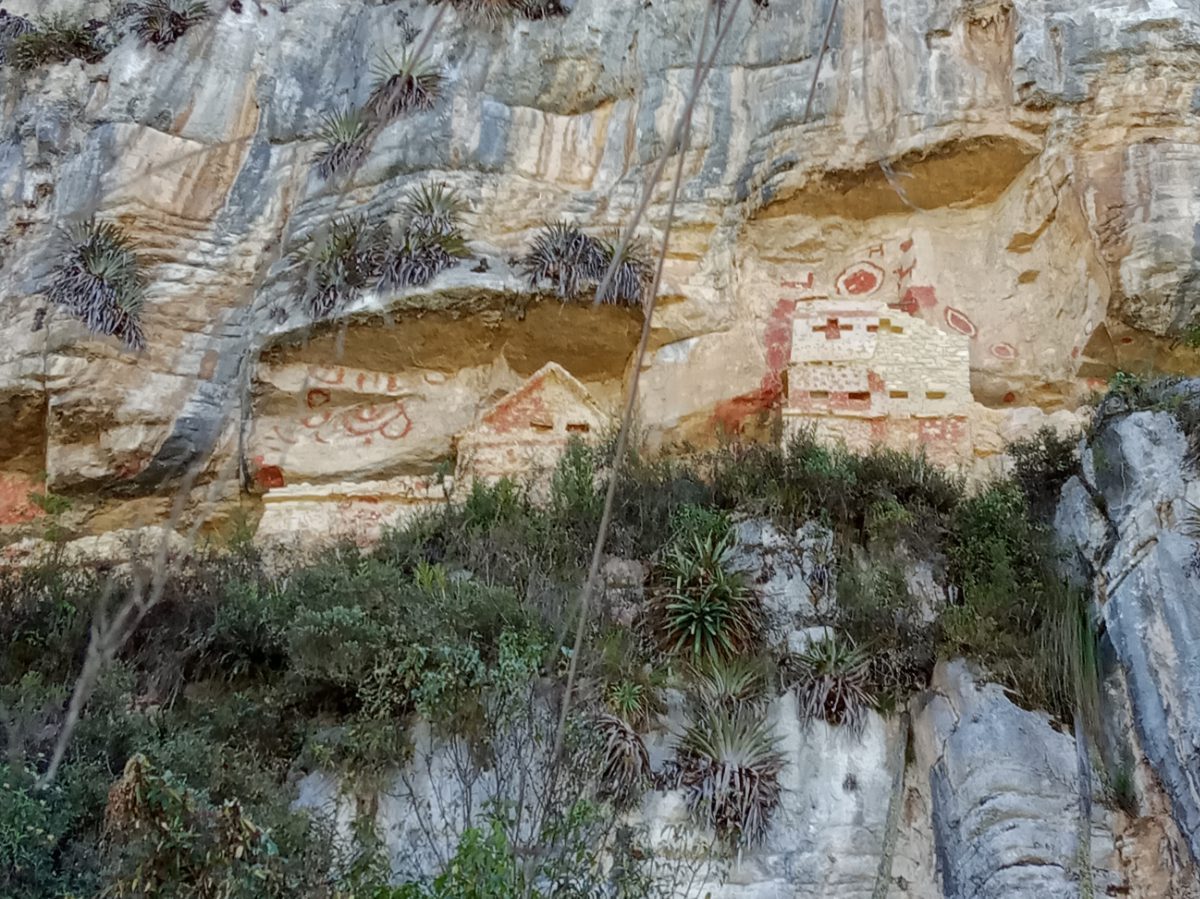 Ancient walls and painted images sit on a ledge on a gray and yellow mountain 