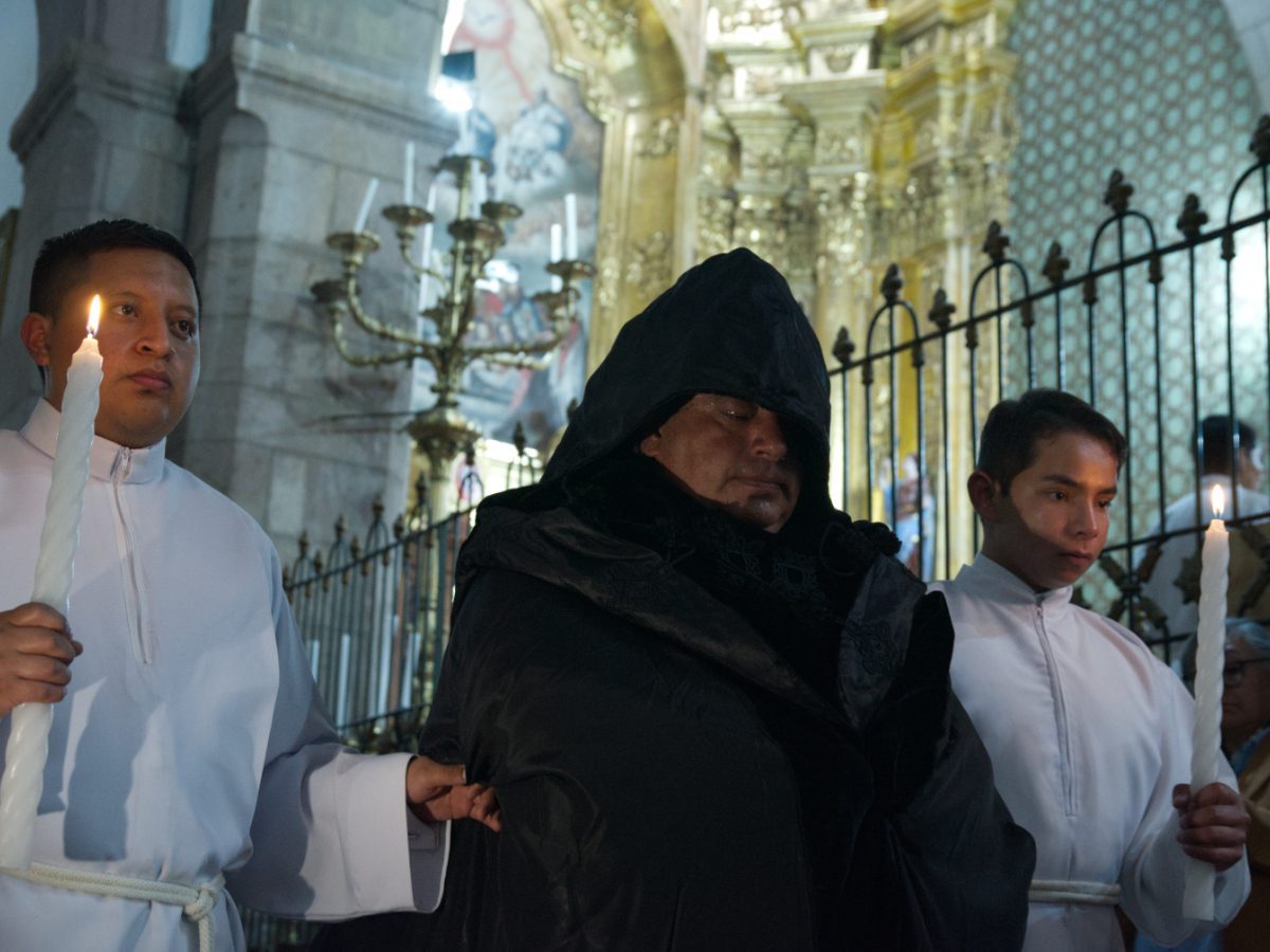 Priest in black robes escorted by two white-robed acolytes during Arrastre de Caudas procession in Quito