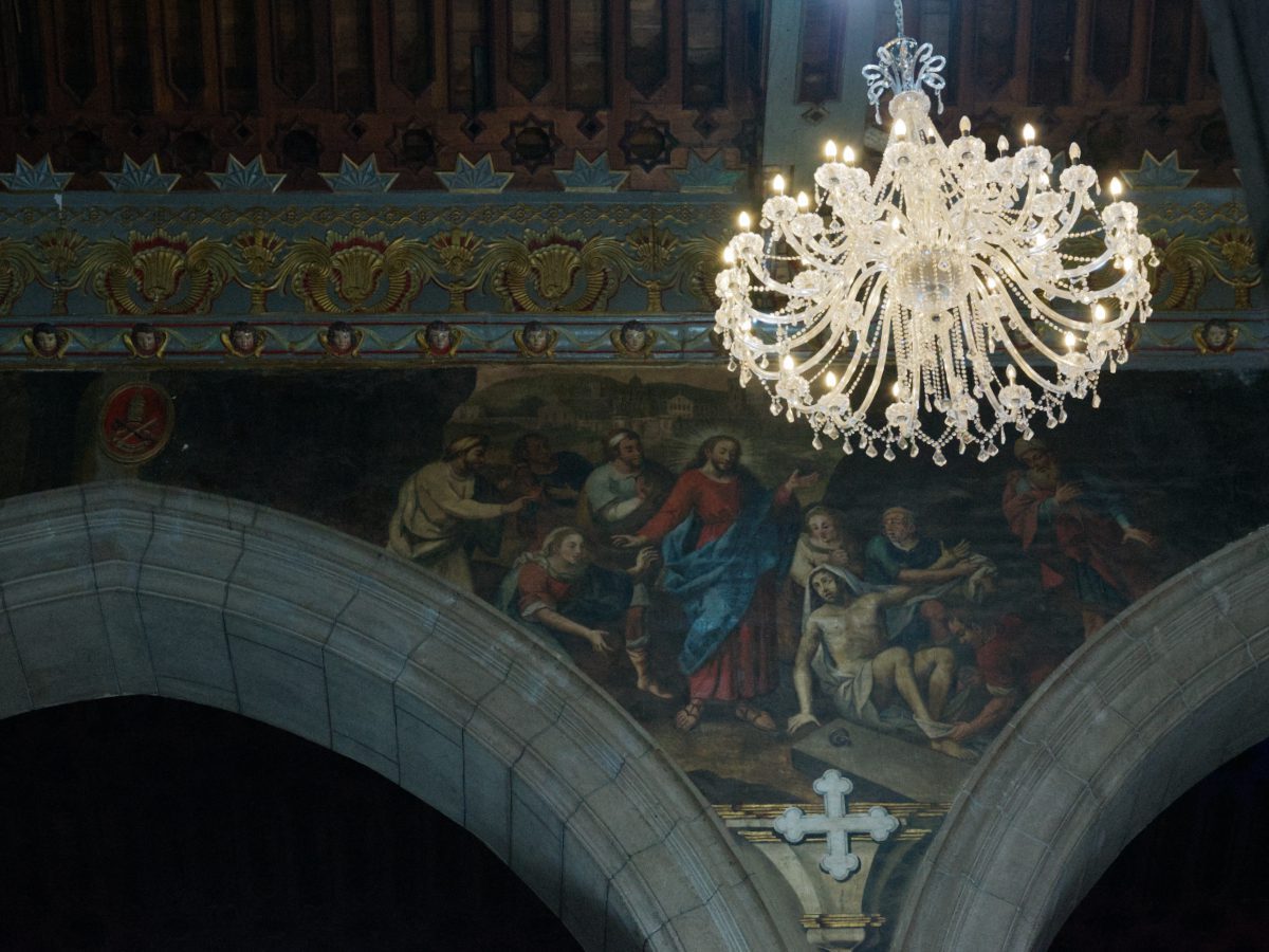 A brilliant white chandelier commands attention against the darker mural painted on the walls of the Quito Cathedral