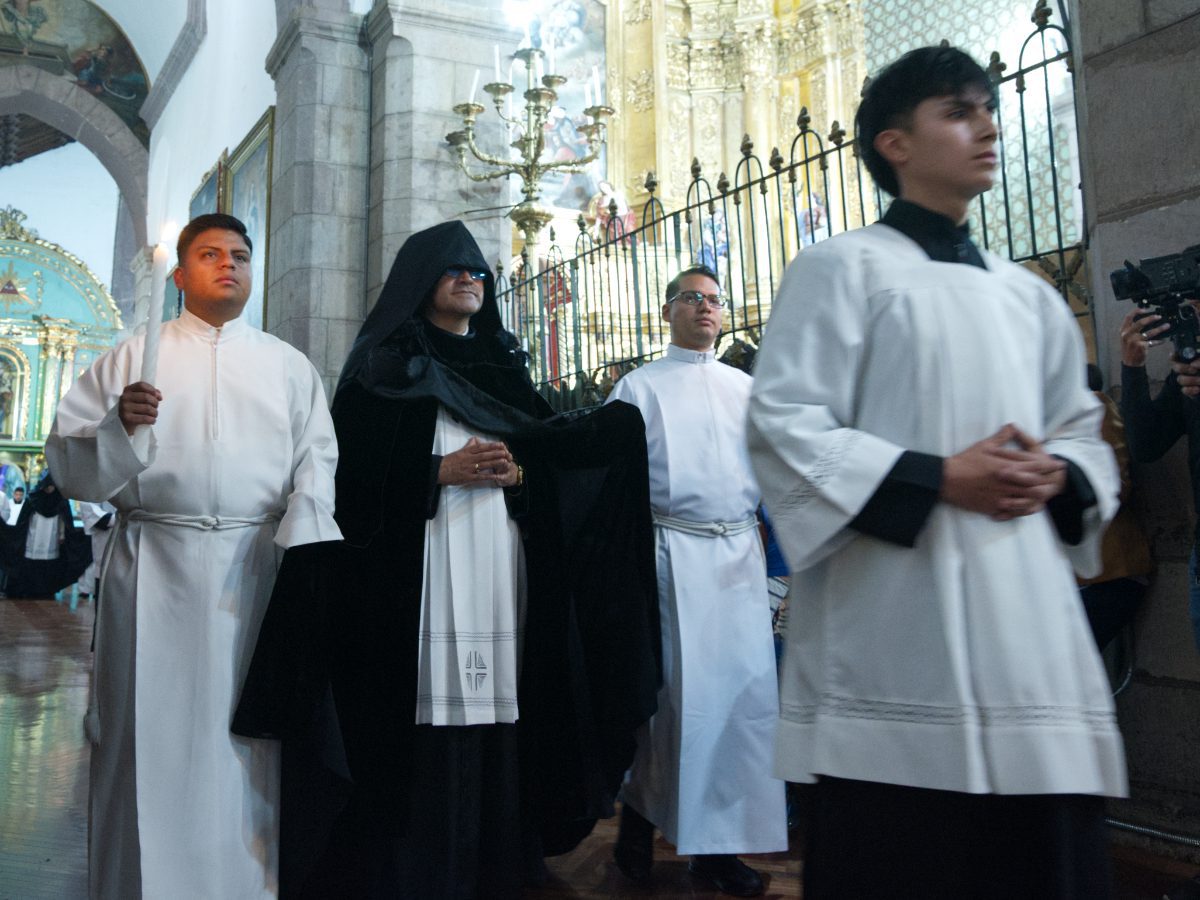 Black-robed canon with long train walking past press, escorted by acolytes, Quito Holy Week ceremony